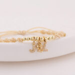 Pulsera De Oro 18k Con 6 Esferas 4mm 2 Esferas 5mm, Hilo Color Beige Dijes Letra J y L y Dije Tres Gracias