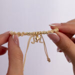 Pulsera De Oro 18k Con 6 Esferas 4mm 2 Esferas 5mm, Hilo Color Beige Dijes Letra J y L y Dije Tres Gracias - Imagen 2